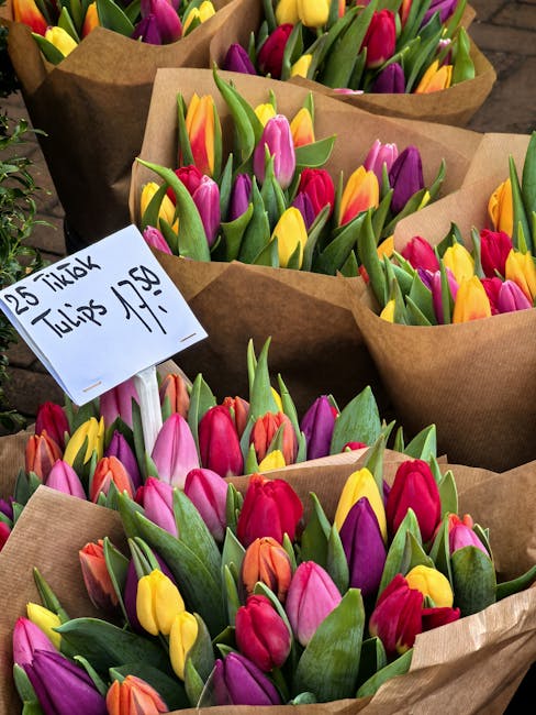 A display of assorted fresh floral bouquets arranged in metal buckets at a flower shop, featuring a variety of flowers including pink roses, orange and yellow tulips, and mixed pink and peach blossoms